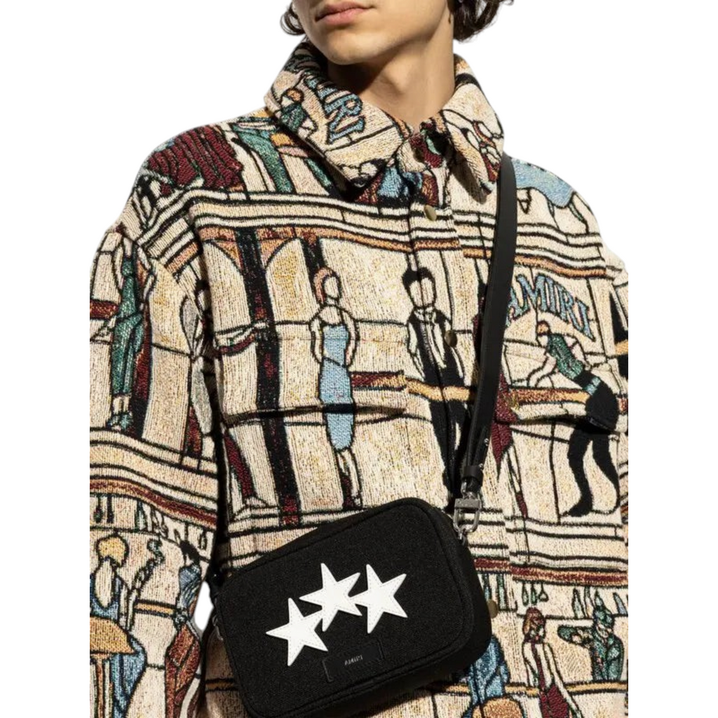 FLEX SHOP Amiri black messenger bag with white three-star detailing worn across the body by a model